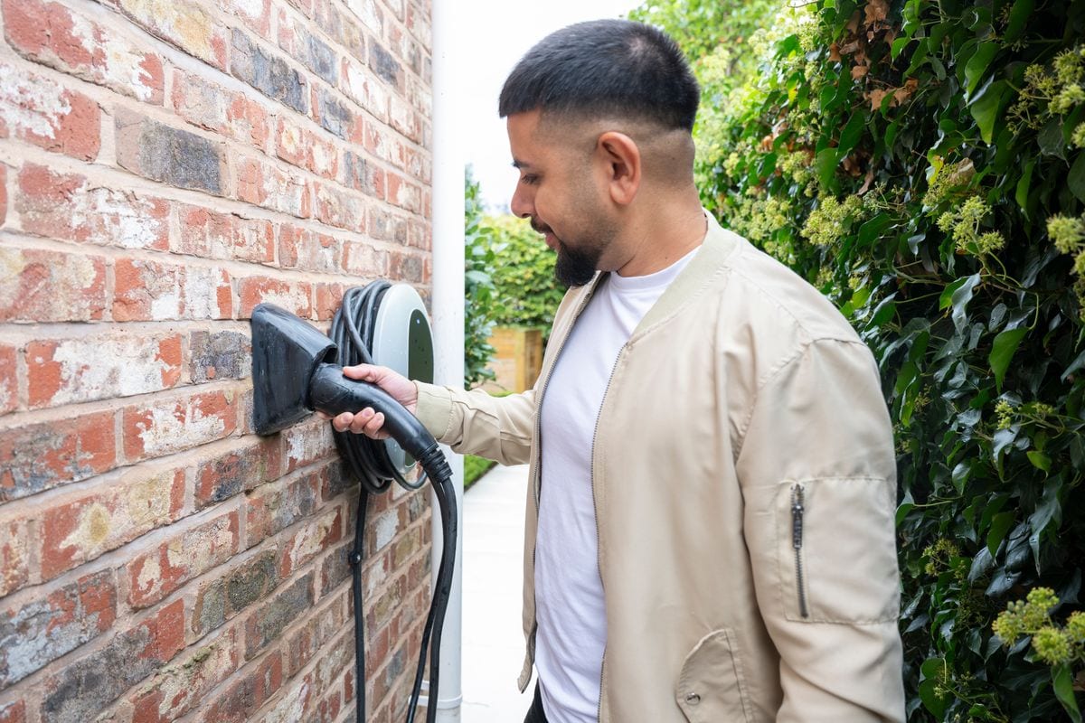 Man in his 30s holding an EV charging cable outside house, sustainability, electricity, green issues