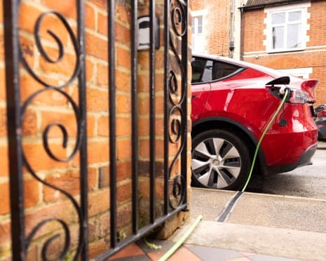 A charge gully with a car on charge in the street with a metal gate open against a brick wall in the foreground