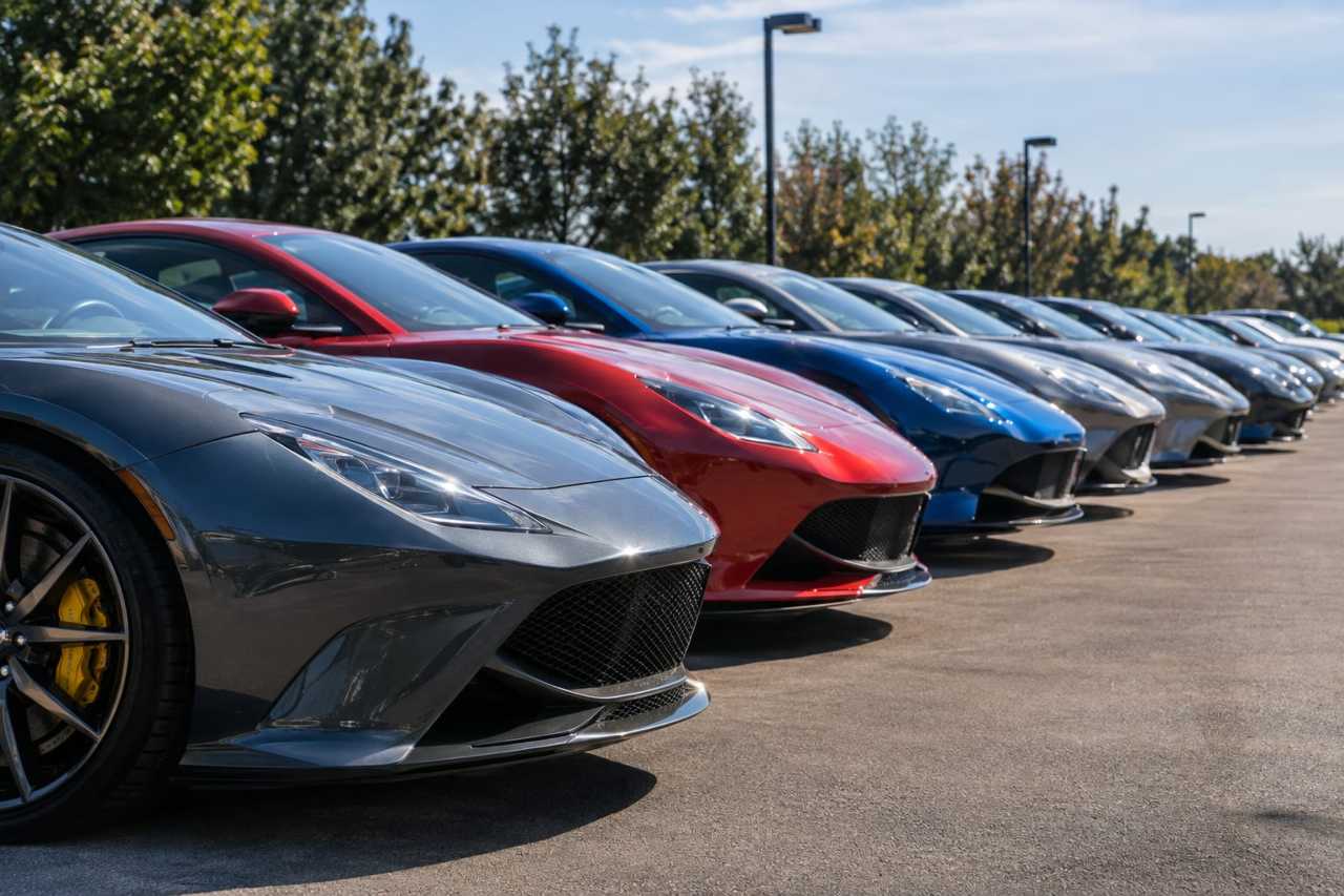 Unsold luxury sedans line a quiet dealership lot.